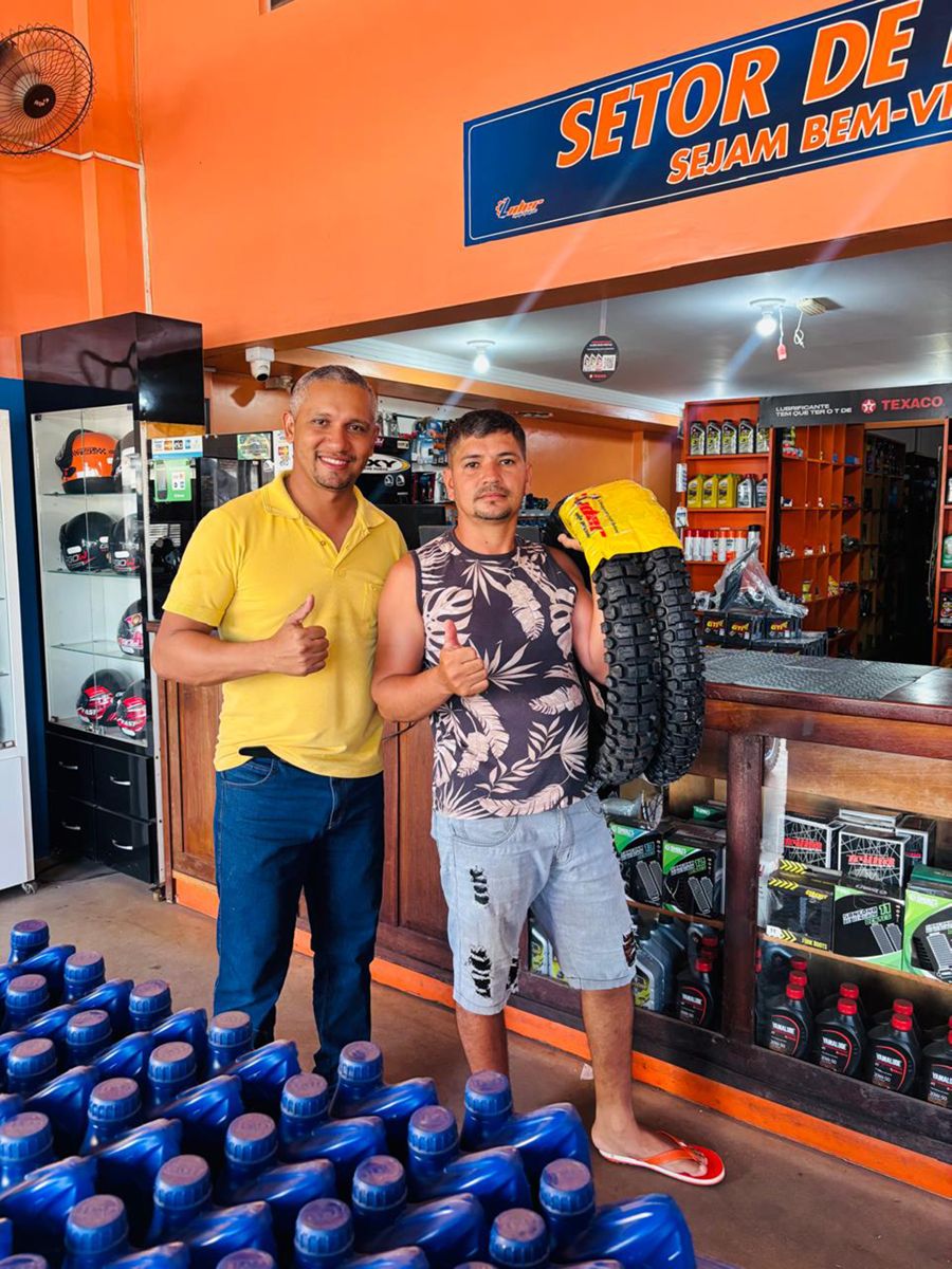 Cliente satisfeito com pneus novos na loja, ao lado da vitrine de capacetes